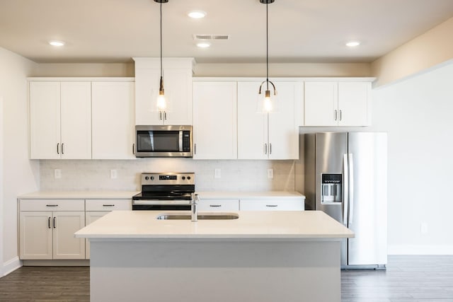 kitchen with appliances with stainless steel finishes, white cabinetry, pendant lighting, and an island with sink