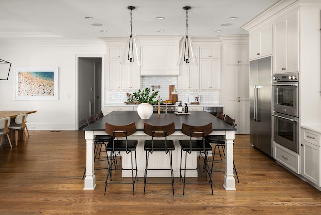 kitchen with white cabinets, an island with sink, decorative light fixtures, and appliances with stainless steel finishes