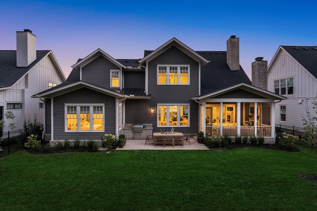 back house at dusk with a lawn, a sunroom, and a patio