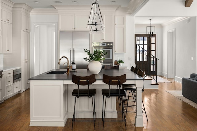 kitchen featuring pendant lighting, built in appliances, white cabinetry, and sink