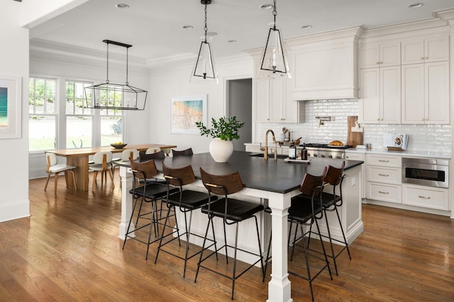 kitchen featuring backsplash, premium range hood, dark wood-type flooring, a center island with sink, and white cabinetry