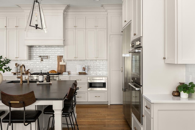 kitchen with backsplash, dark wood-type flooring, hanging light fixtures, white cabinetry, and stainless steel double oven