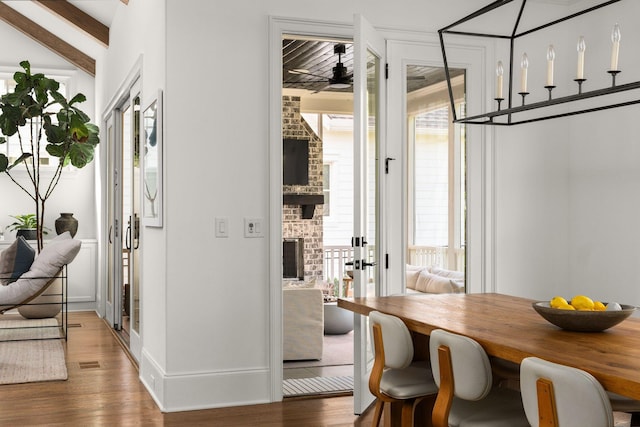 dining room featuring beamed ceiling, dark hardwood / wood-style flooring, a brick fireplace, and a wealth of natural light