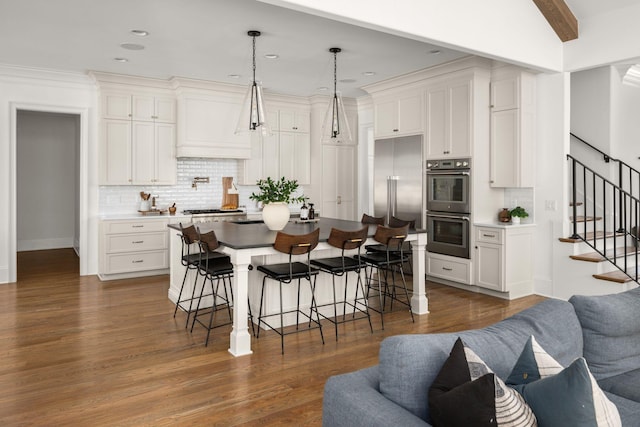 kitchen featuring appliances with stainless steel finishes, custom exhaust hood, beam ceiling, white cabinets, and hanging light fixtures