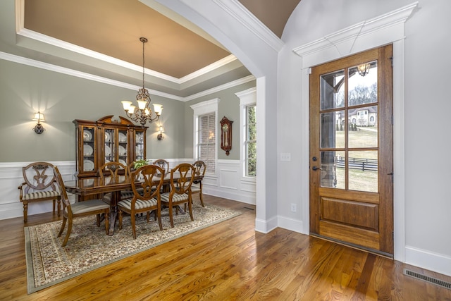 dining space with a raised ceiling, wood-type flooring, crown molding, and a chandelier