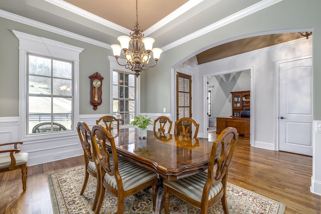 dining space with a raised ceiling, wood-type flooring, ornamental molding, and a chandelier