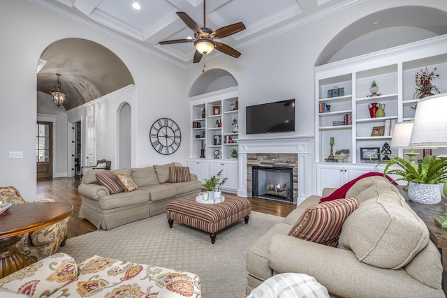 living room featuring a stone fireplace, coffered ceiling, built in features, and light hardwood / wood-style flooring