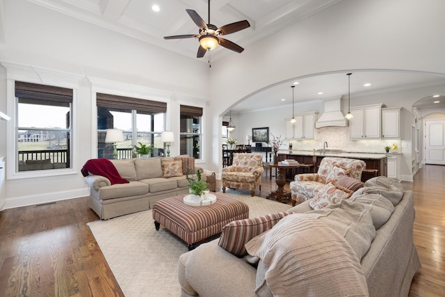 living room featuring crown molding, dark wood-type flooring, ceiling fan, a towering ceiling, and coffered ceiling