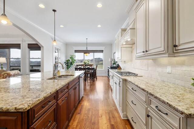 kitchen with ornamental molding, light stone countertops, sink, and hanging light fixtures