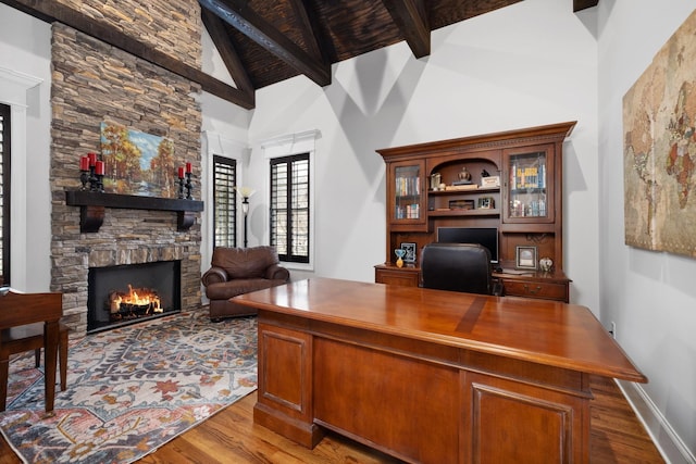 office featuring beam ceiling, a stone fireplace, wood-type flooring, and high vaulted ceiling