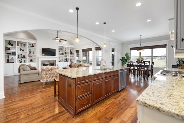 kitchen featuring appliances with stainless steel finishes, pendant lighting, a fireplace, light stone countertops, and a center island with sink