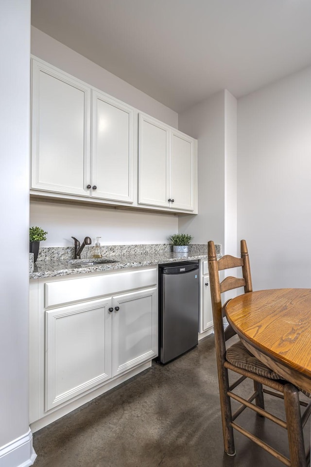 kitchen featuring white cabinetry, fridge, light stone countertops, and sink