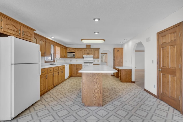 kitchen with sink, a textured ceiling, white appliances, a breakfast bar area, and a kitchen island