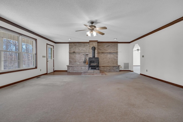 unfurnished living room with carpet, ceiling fan, a wood stove, and crown molding