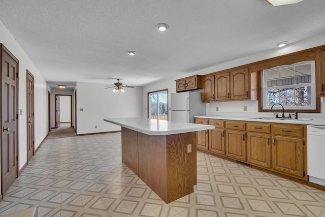 kitchen with ceiling fan, sink, a textured ceiling, white appliances, and a kitchen island