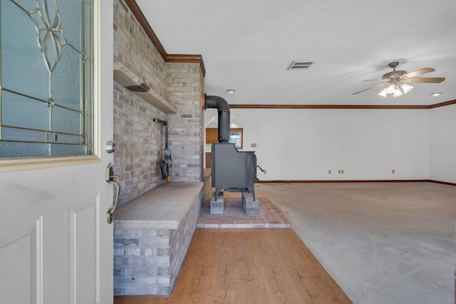 interior space with a wood stove, ceiling fan, light hardwood / wood-style flooring, and crown molding