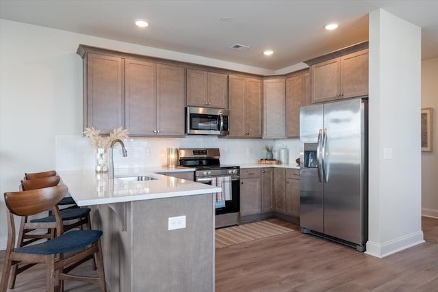 kitchen featuring kitchen peninsula, appliances with stainless steel finishes, a kitchen bar, backsplash, and sink