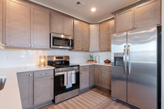 kitchen with decorative backsplash, appliances with stainless steel finishes, and light hardwood / wood-style floors