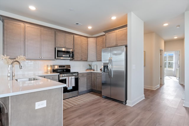 kitchen featuring kitchen peninsula, appliances with stainless steel finishes, tasteful backsplash, sink, and light hardwood / wood-style floors