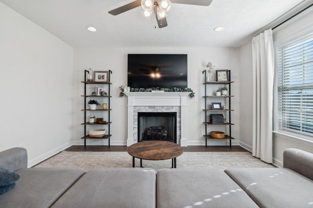 living room featuring a stone fireplace, ceiling fan, and light wood-type flooring