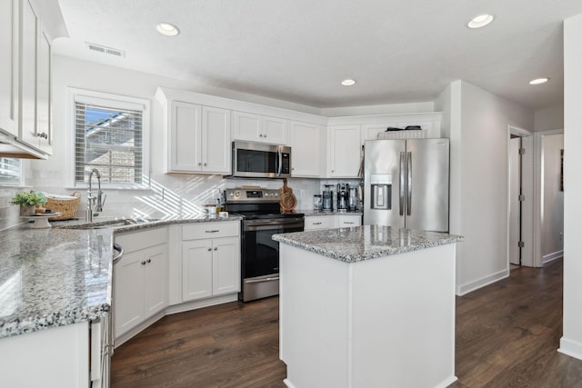 kitchen with white cabinets, a kitchen island, light stone counters, and stainless steel appliances