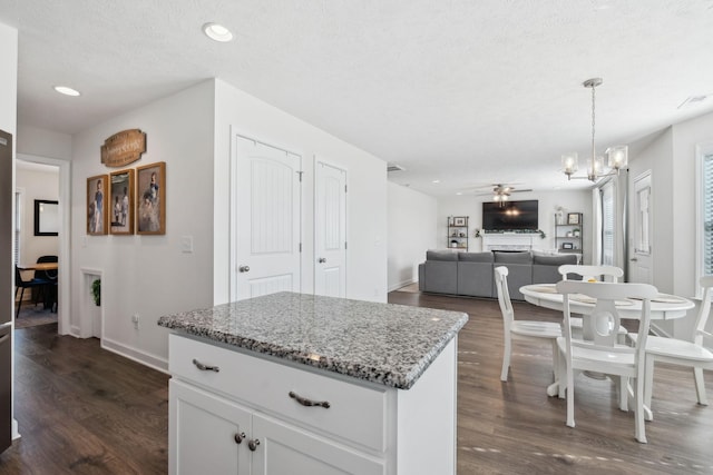 kitchen with light stone countertops, ceiling fan with notable chandelier, a textured ceiling, pendant lighting, and white cabinets