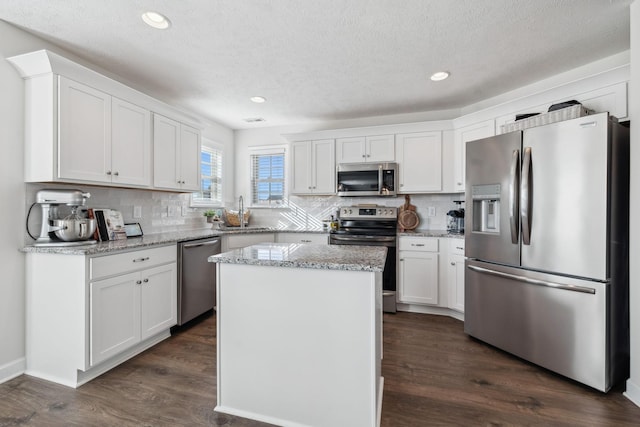 kitchen featuring white cabinetry, a center island, light stone counters, dark hardwood / wood-style flooring, and appliances with stainless steel finishes