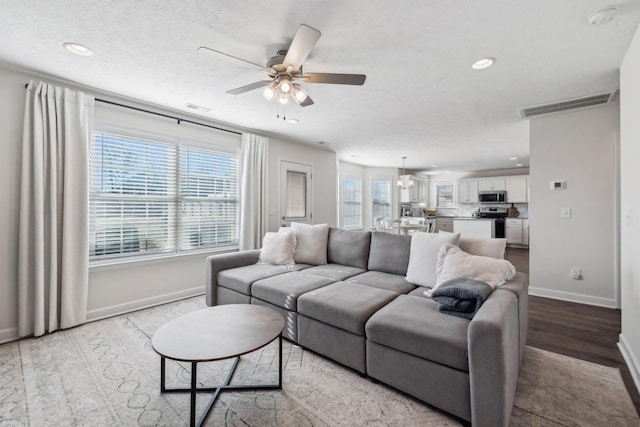 living room featuring ceiling fan with notable chandelier, light wood-type flooring, and a textured ceiling