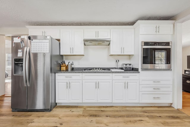 kitchen with appliances with stainless steel finishes, a textured ceiling, dark stone countertops, light hardwood / wood-style floors, and white cabinetry