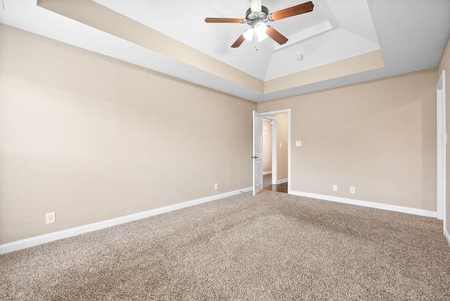 carpeted spare room with a raised ceiling and ceiling fan