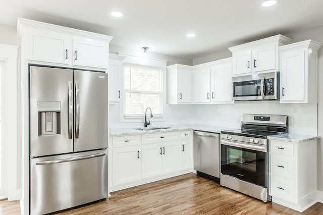 kitchen featuring sink, light hardwood / wood-style flooring, appliances with stainless steel finishes, light stone counters, and white cabinetry