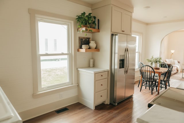 kitchen with stainless steel fridge with ice dispenser, white cabinetry, light hardwood / wood-style flooring, and plenty of natural light