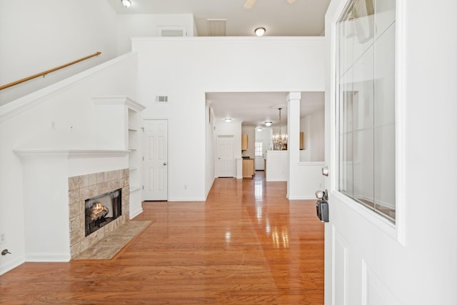 foyer entrance featuring a high ceiling, light hardwood / wood-style flooring, a notable chandelier, decorative columns, and a fireplace