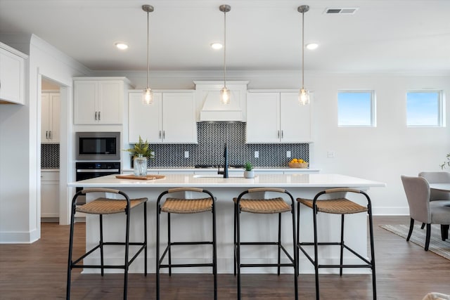 kitchen featuring pendant lighting, white cabinetry, built in microwave, and an island with sink