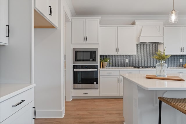 kitchen with white cabinetry, custom range hood, decorative light fixtures, and appliances with stainless steel finishes