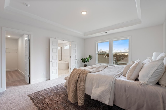 bedroom featuring a tray ceiling, carpet, ensuite bath, and baseboards