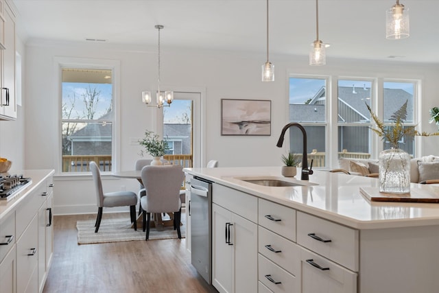 kitchen featuring hanging light fixtures, white cabinets, a kitchen island with sink, and sink