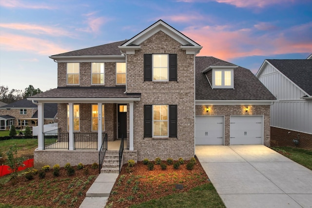 traditional-style home featuring covered porch, a garage, a shingled roof, brick siding, and driveway