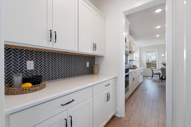 kitchen featuring white cabinets, backsplash, light hardwood / wood-style flooring, and stainless steel oven