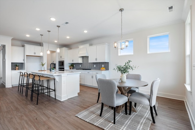 kitchen with white cabinetry, hanging light fixtures, and an island with sink