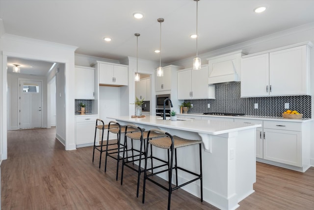 kitchen with white cabinets, pendant lighting, premium range hood, and a center island with sink