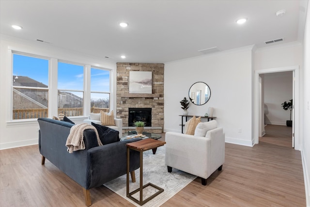 living area featuring light wood-style floors, visible vents, a stone fireplace, and ornamental molding