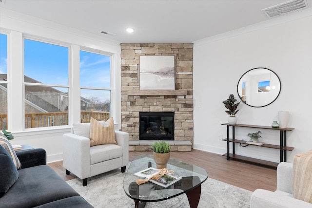 living area featuring visible vents, crown molding, a stone fireplace, and wood finished floors