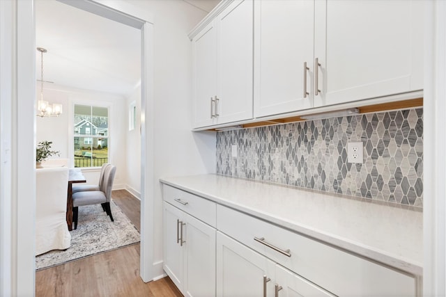 bar with light wood finished floors, tasteful backsplash, baseboards, pendant lighting, and a notable chandelier