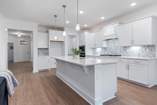 kitchen with a center island with sink, appliances with stainless steel finishes, light wood-style floors, white cabinets, and premium range hood