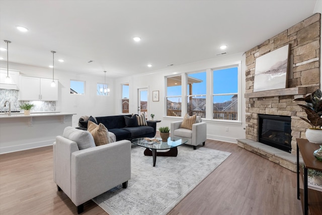 living room featuring light wood-type flooring, recessed lighting, baseboards, and a stone fireplace