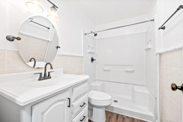 bathroom featuring vanity, a shower, hardwood / wood-style flooring, tile walls, and toilet