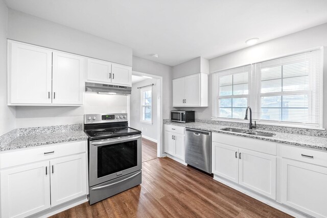 kitchen featuring light stone countertops, stainless steel appliances, sink, dark hardwood / wood-style floors, and white cabinetry