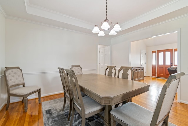 dining space with a tray ceiling, light hardwood / wood-style flooring, ornamental molding, and an inviting chandelier