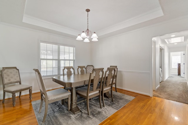 dining space featuring hardwood / wood-style floors, an inviting chandelier, a raised ceiling, and ornamental molding